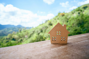 Obraz na płótnie Canvas Small model home on wooden table with mountain view and blue sky white cloud abstract background.