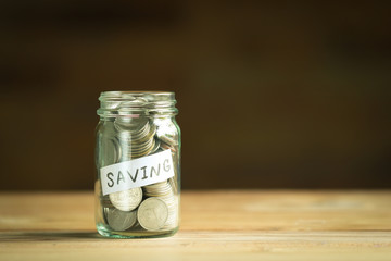 Coins in the glass jar on the table with vintage filter.