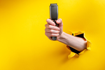 Hand showing a electric shaver through torn yellow paper background