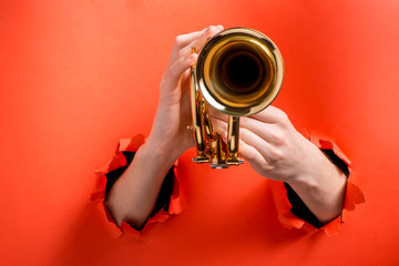 Hands playing trumpet through torn red paper background