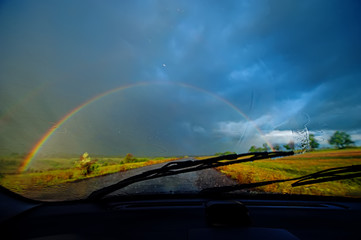 View of a Car Windshield and Landscape and Rainbow During Heavy Rain, Blurred background. 