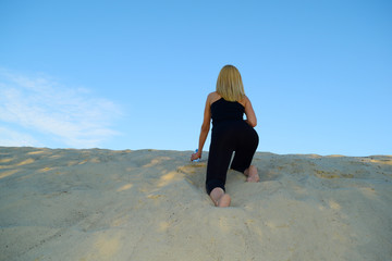 Rear view of a sporty girl crawling on sand in the desert