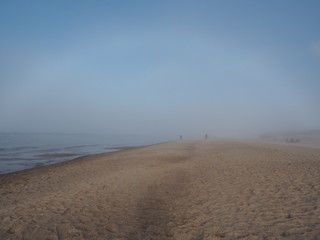 Footprints in the sand of the seashore. Light fog. Blue sky.