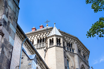 Germany, Cologne: Famous old St. Gereon's Basilica in the city center of the German town from below with green trees and blue sky - concept religion Christianity cathedral church travel architecture