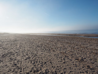 Footprints in the sand of the seashore. Light fog. Blue sky.