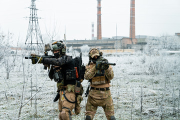 Men in camouflage cloth and black uniform with machineguns with factory on background. Soldiers...