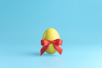 One yellow easter egg  with a red ribbon bow on a blue background. Minimal Happy Easter concept decoration. Copy space for text mockup.