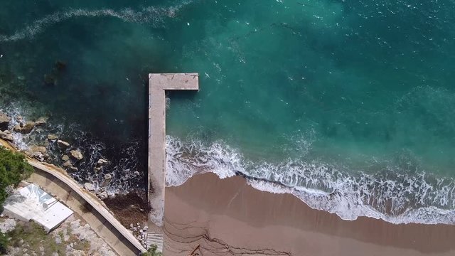Aerial drone top view at stone pier breakwater, turquoise water in sea, waves, beach with brown sand is emty.