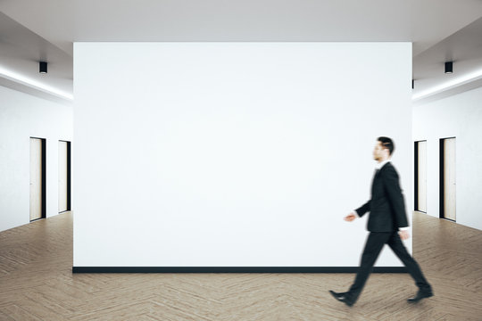 Businessman walking in clean hall interior with blank white wall