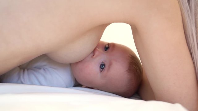 Woman breastfeeding newborn baby. Mother breastfeeding newborn boy lying in bed. Concept breast feeding. Baby eating mother's milk. Young woman nursing and feeding baby. Concept of lactation infant.