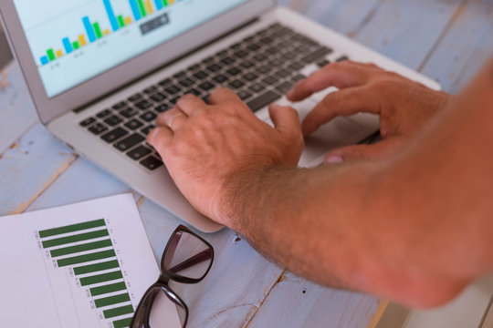 close up of hands of man using a laptop - business man looking at the graphs on the screen and on the table