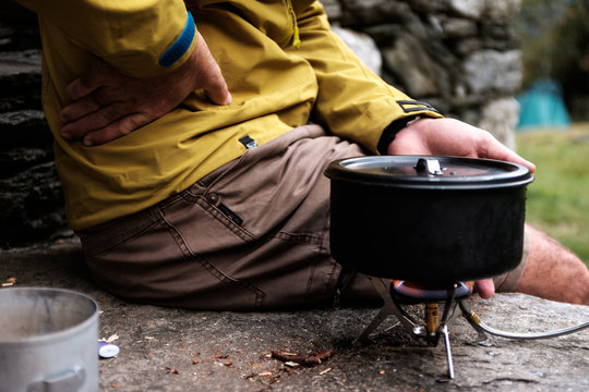 Side view of a man sitting near a camping stove heating his hands 