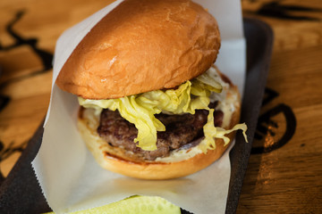 Burger with cutlet, cabbage and cucumber in a white paper envelope on the substrate, on a wooden table, top view.