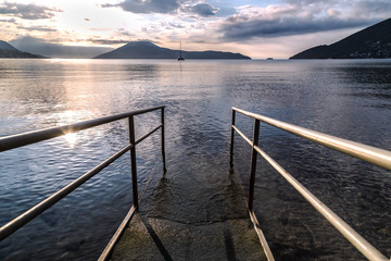 Obraz premium The pier on the sea against sunset sky and mountains in the background. Kotor Bay, Montenegro.