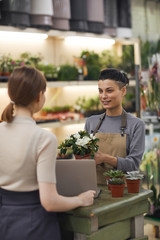 Waist up portrait of modern young woman selling flowers to customer in flower shop and smiling...