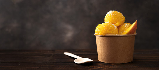 Mango sorbet in a craft paper cup with wooden spoon - obrazy, fototapety, plakaty
