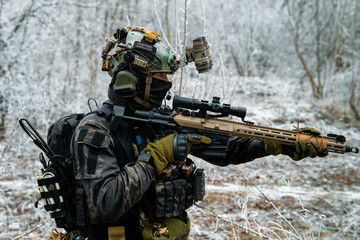 Airsoft man in black camouflage uniform with machinegun. Soldier in the winter forest. Vertical photo.