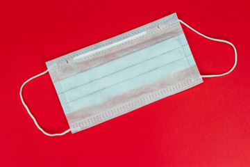 Surgical mask with rubber ear straps — virus concept on red background. Image of a blue face protective mask. Procedure mask from bacteria. Protection concept.