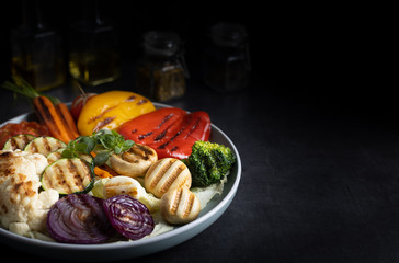 Fresh organic grilled vegetables bell pepper,mushrooms,broccoli,cauliflower,carrots seasoned with herbs on a round plate.