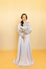 Fototapeta premium Girl in a wedding dress. Minimalism at a wedding photo shoot. Beautiful bride in the Studio on a yellow background.