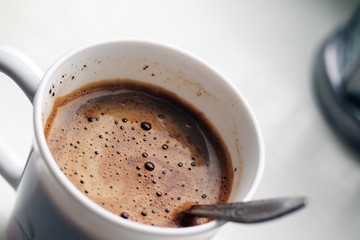 black coffee with foam in white mug with metal vintage spoon