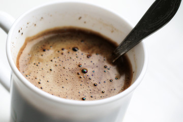 black coffee with foam in white mug with metal vintage spoon