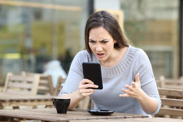 Angry girl looking at her phone on a restaurant terrace
