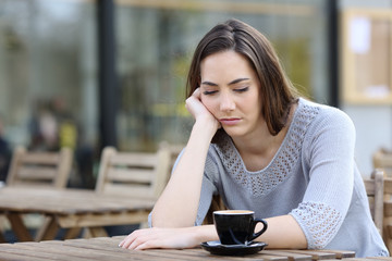 Sad girl looking down pensive on a cafe terrace