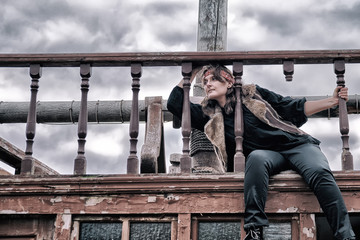 Young woman pirate in vintage clothes sits on the decks of an old wooden ship