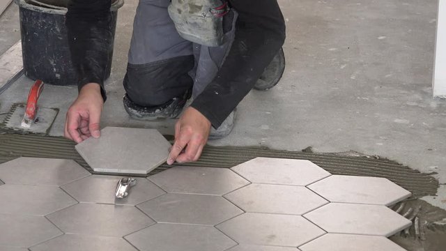 worker laying hexagon stone mass tiles on floor.
