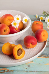 Delicious ripe apricots in a bowl on the wooden table. Close-up with apricots and daisy flowers