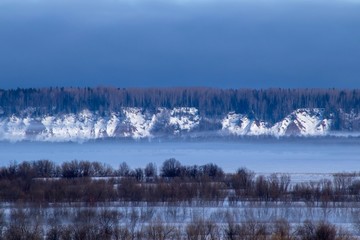 winter landscape with trees and fog over a frozen river