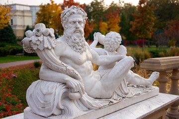 White statue of lying naked man in a park. Sculpture of serious bearded man outdoors.