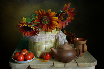 Still life with large sunflowers in a vase and ripe red volumes on a plate on a brown background