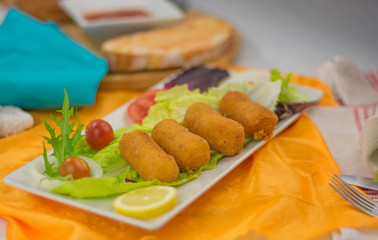 four chicken croquettes in a bowl with lettuce garnish tomatoes bread with tomato and oil