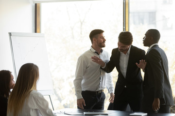 Millennial businessman setting apart two aggressive multiracial coworkers, starting fighting at...