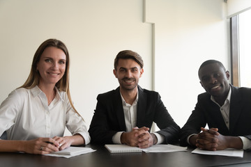 Head shot smiling confident mixed race business team looking at camera, holding video call with partners, clients or investors. Diverse teammates making corporate conference call at workplace.