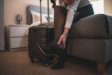 Overworked businesswoman on business trip sitting in hotel room and  having pain in leg.