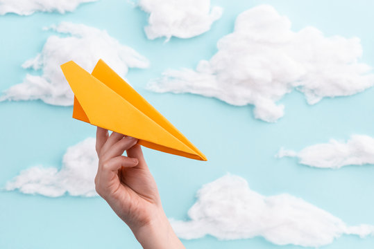 Orange paper airplane in child's hand flying on blue sky background