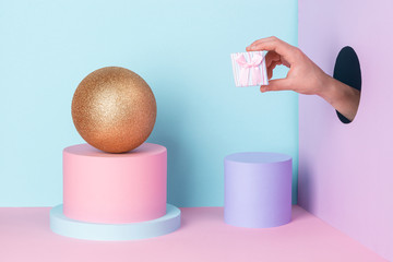 Hand showing a tiny gift box through a hole in the wall