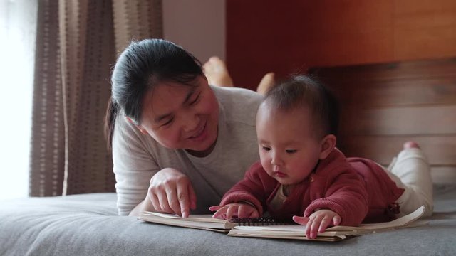 Slow motion of asian woman telling her baby infant daughter story at bedroom lying in bed story time with mother early education of infant development 