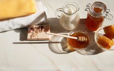 Natural home skin care. The pleasure of taking a bath. Sweet Golden honey, milk, handmade soap with olive oil and clean towels on a pastel green marble background. The soft sunlight.