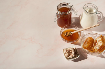 Natural home skin care. Ingredients for the mask. Sweet Golden honey, a jug of milk and natural live yeast on a pink marble background. The soft sunlight. Free space. Copy space.