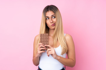 Young Uruguayan woman over isolated pink background taking a chocolate tablet and having doubts