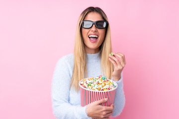 Young Uruguayan woman over isolated pink background with 3d glasses and holding a big bucket of popcorns while pointing front