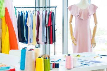 Fashion designer working desk with colorful sewing thread, colored pencils and fabric sample including mannequin and hanging clothes at the office or studio
