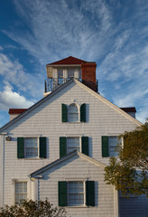 A nice coastal home under clear blue skies with white wood siding and green shutters