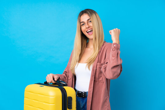Young Uruguayan woman over isolated blue background in vacation with travel suitcase and a hat