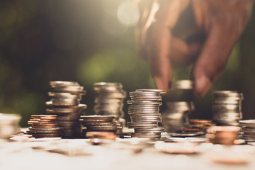 Numerous coins were stacked, with the hands of a man picking up the coins while the morning sun was...