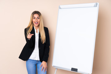 Young Uruguayan woman giving a presentation on white board and surprised while pointing front
